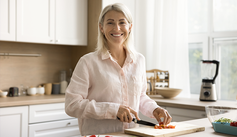 Mulher de meia-idade sorrindo enquanto corta ingredientes na cozinha para preparar uma refeição